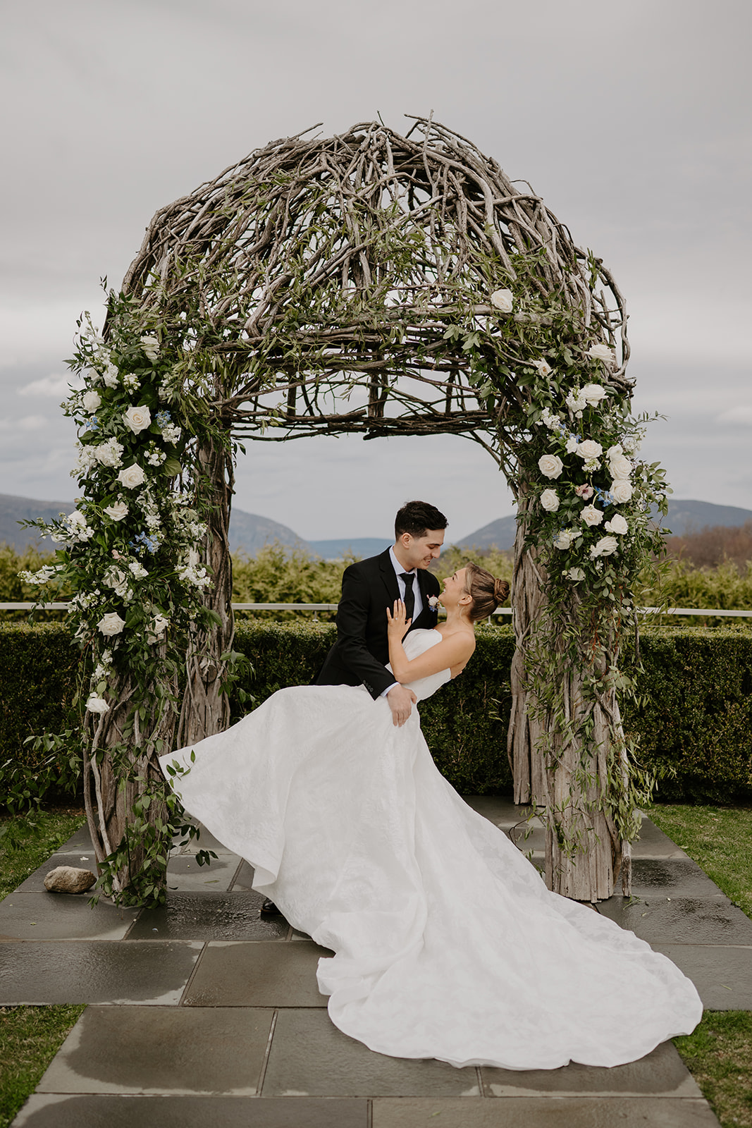 Color photo showing the groom dipping the bride under the decorated rustic ceremony arch at The Garrison in Garrison, NY.