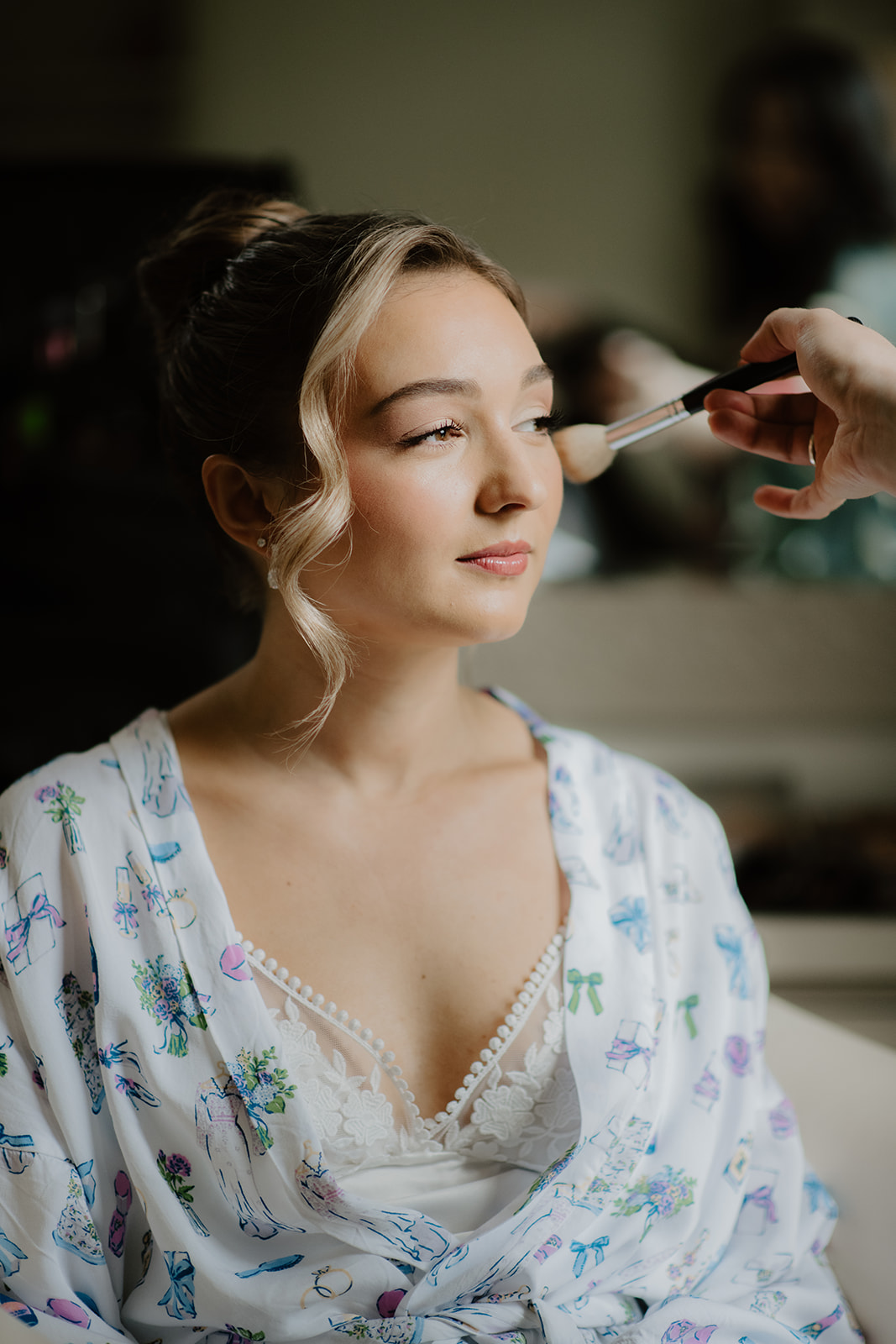 Bride getting ready candid smiling as makeup artist applies finishing touches.