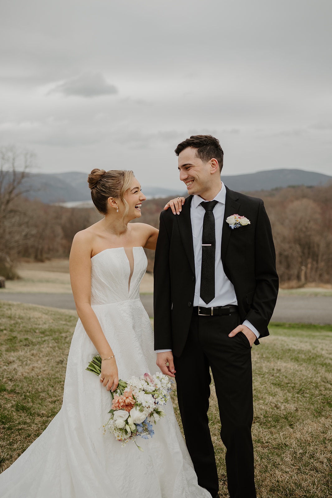 Couple standing on the grass, the bride laughing with her hand on the groom's shoulder.