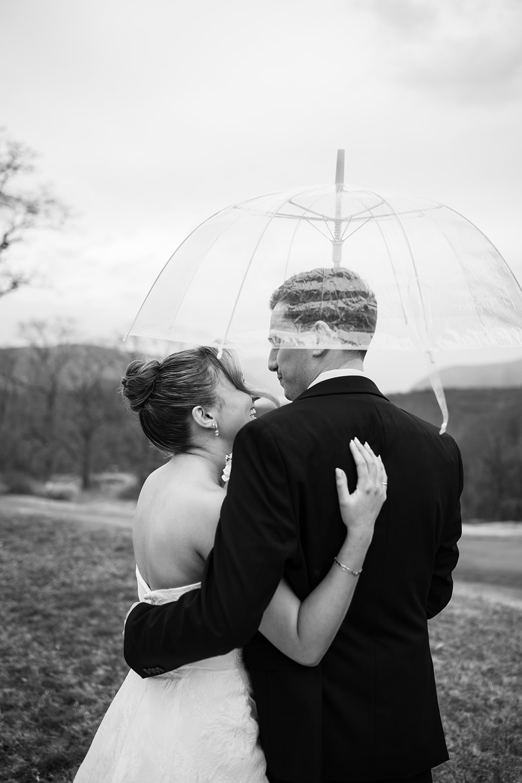 Black and white photo of the couple standing together under a clear umbrella.