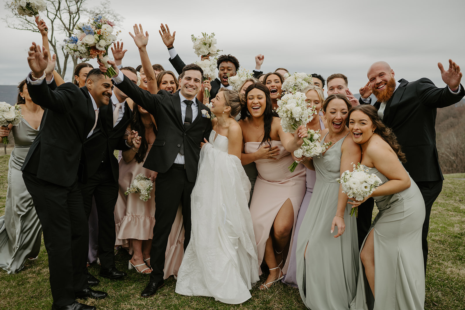 Wedding party group-hugging the couple and raising their bouquets in celebration.