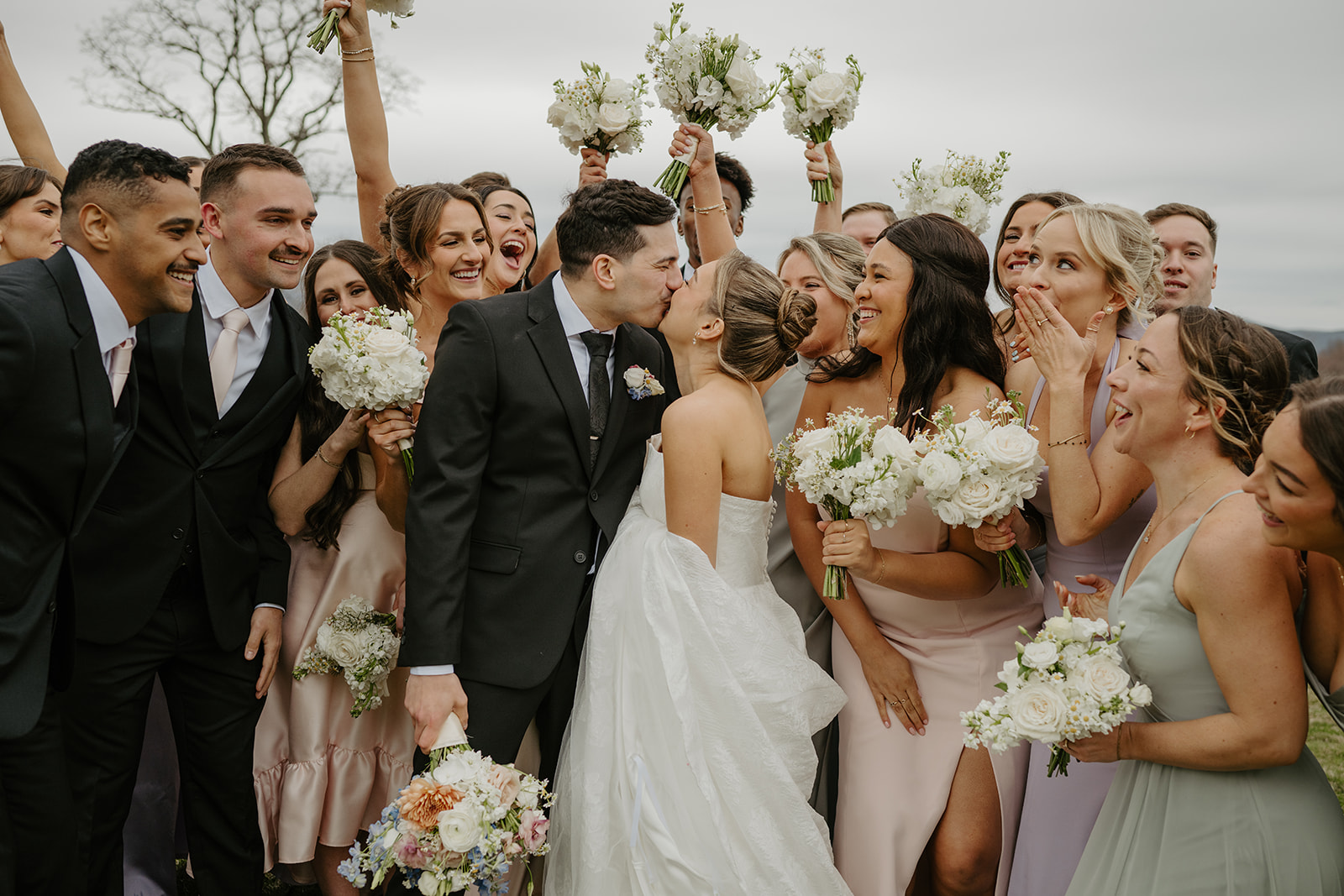 Close-up of the couple kissing with the wedding party holding their bouquets around them.