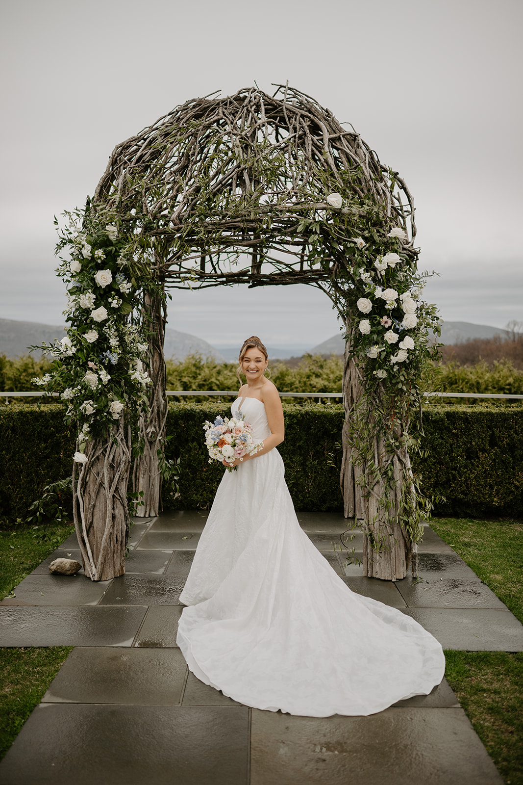 Bride standing under the ceremony arch, showing her full wedding dress and train.