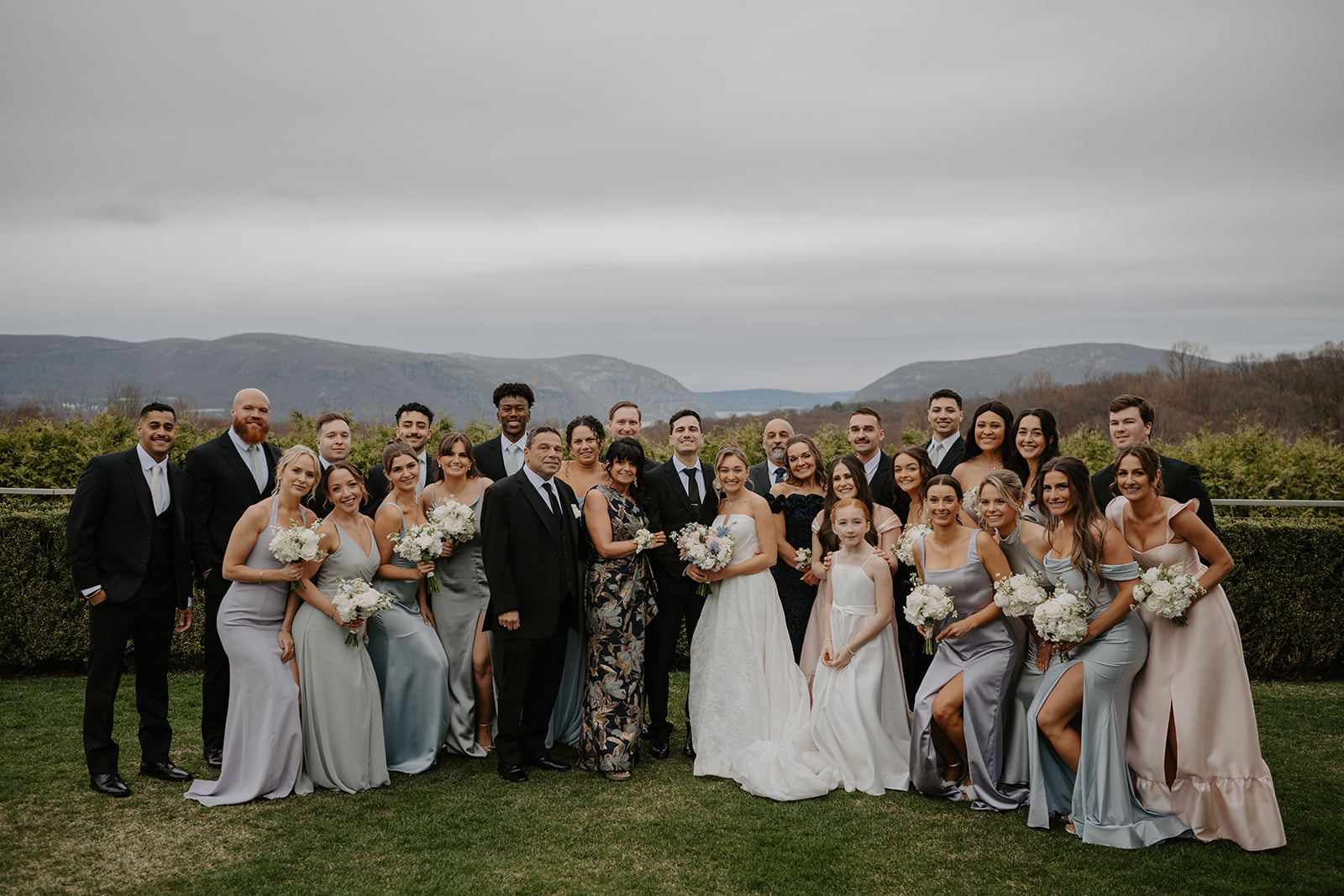 Couple, parents, and the full wedding party posing together on the lawn.