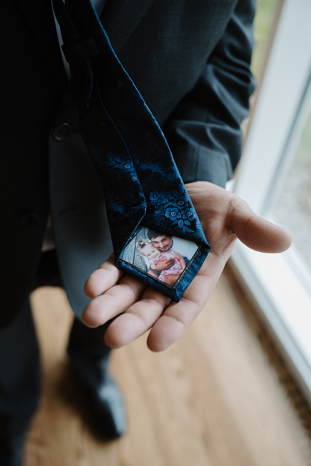 Close-up detail of the groom's tie, featuring a small charm with a childhood photo.