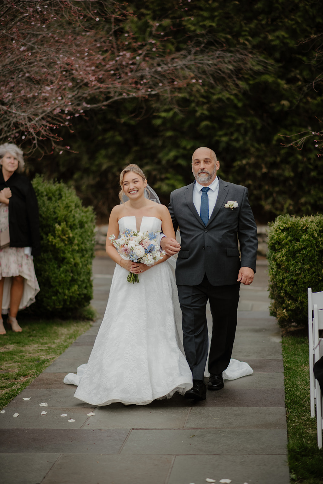 Bride walking down the aisle with her father, smiling at guests.