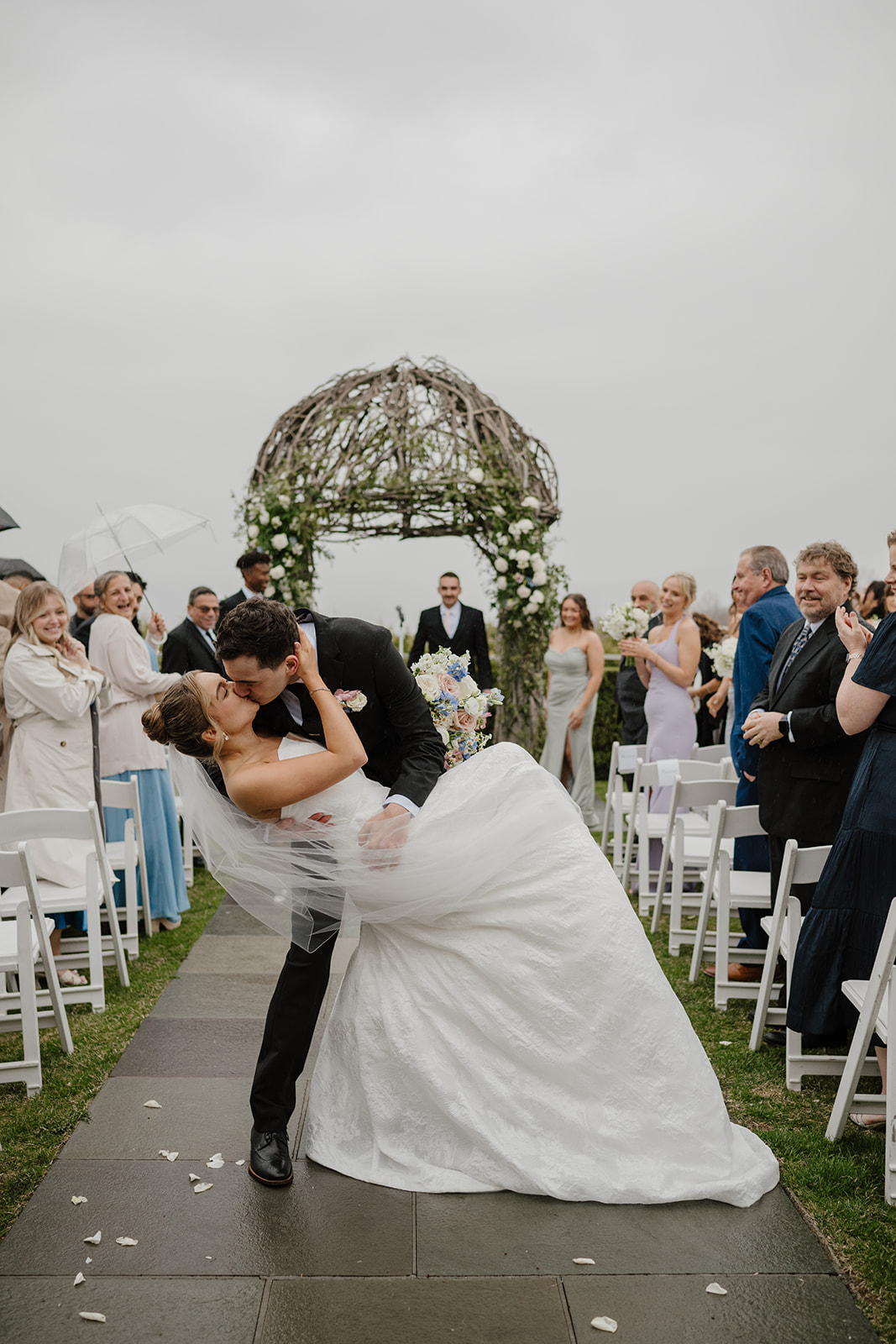 Newlyweds recessional dip kiss on the ceremony aisle, guests cheering in the background.
