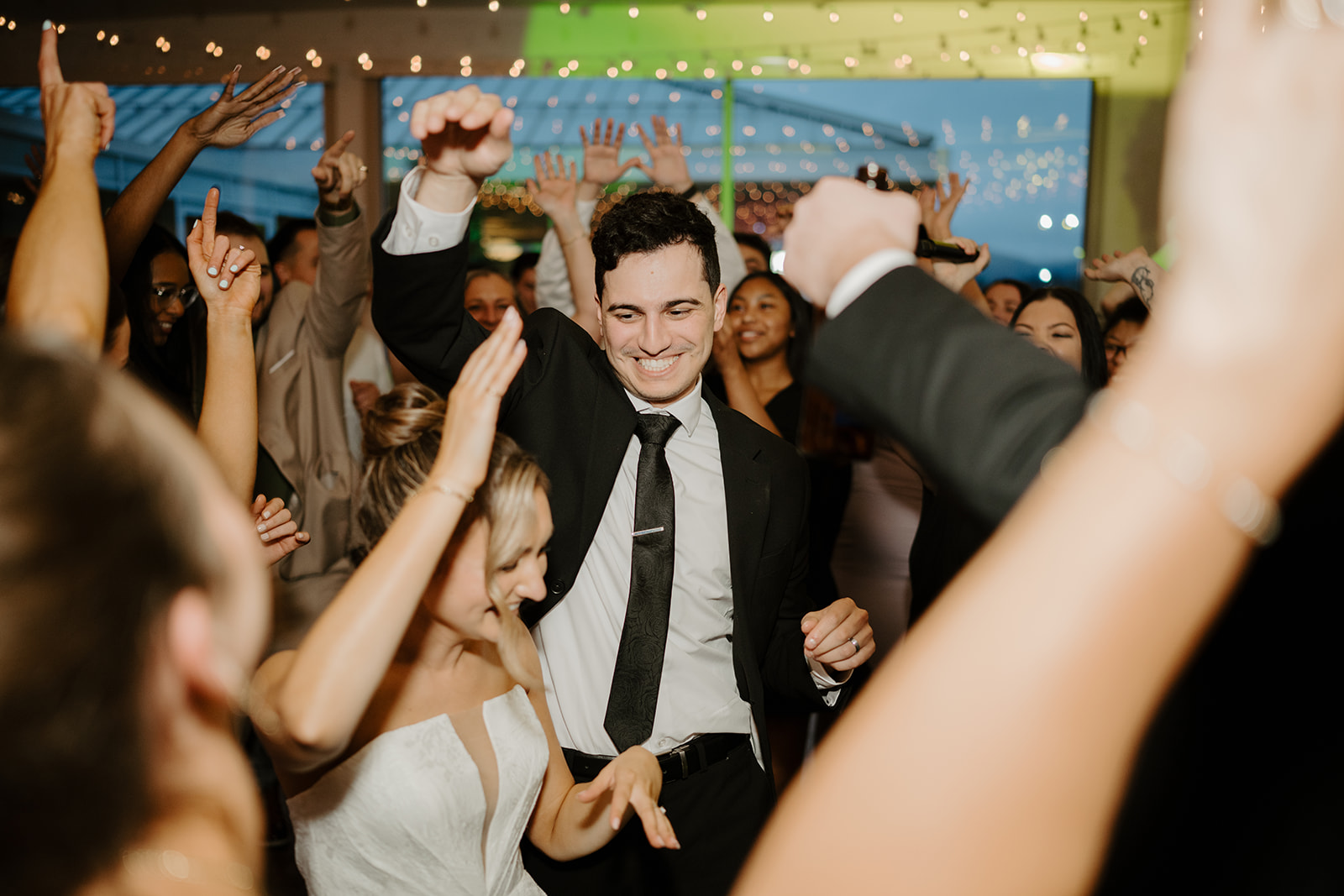 Bride and groom dancing energetically on the packed dance floor surrounded by cheering guests.