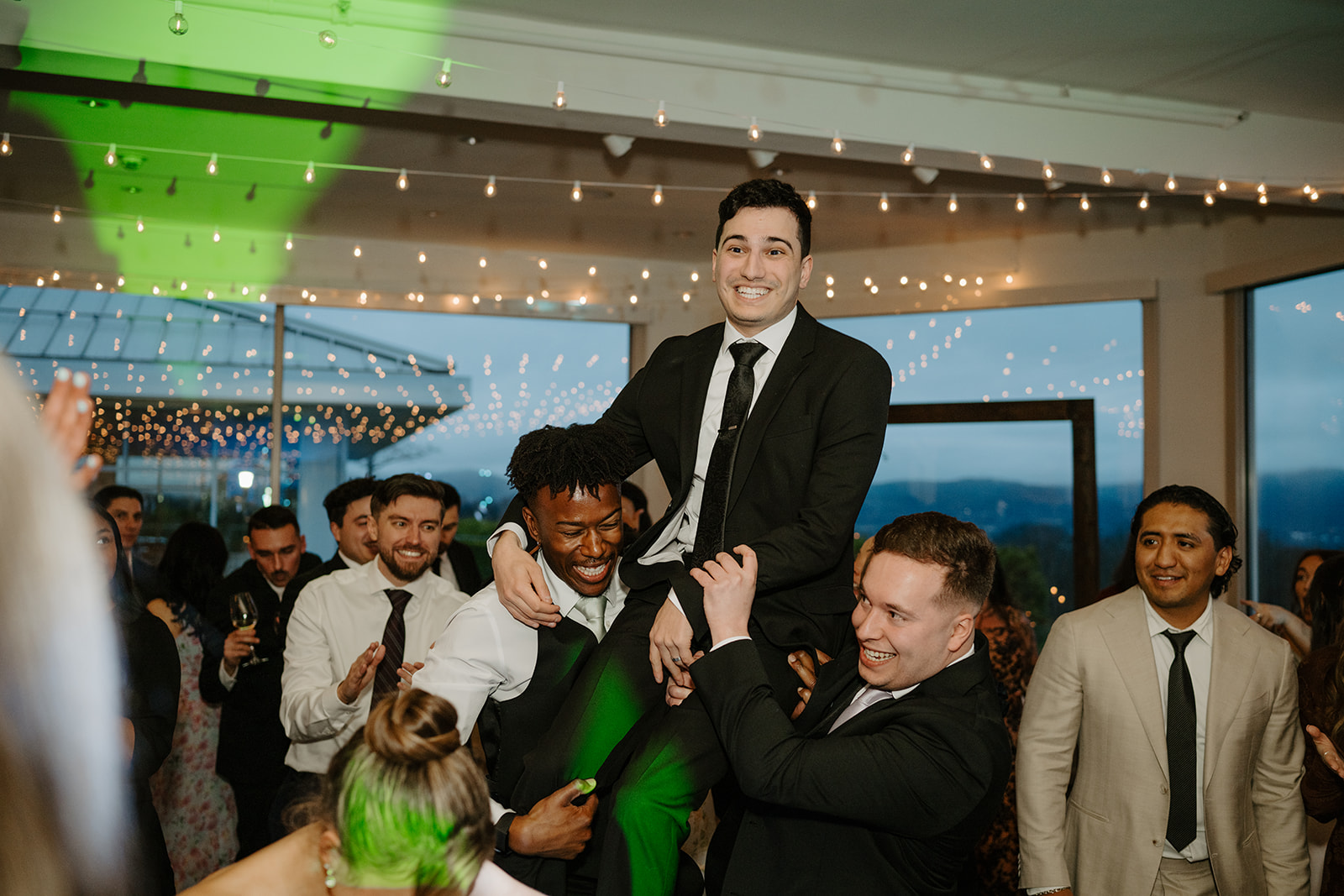 Groom smiling broadly while being lifted on the shoulders of his groomsmen during the reception dance party.