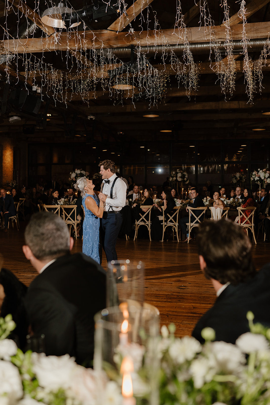 Groom dances with his mother under shimmering fairy lights on the reception dance floor.
