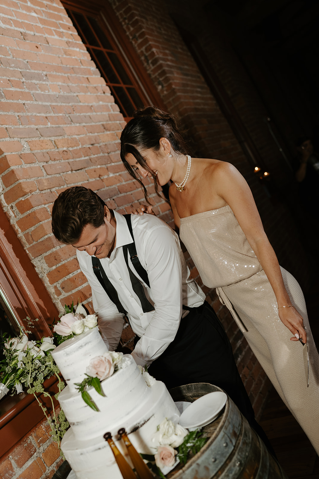 Bride and groom cut their three-tiered wedding cake displayed on a wooden wine barrel.