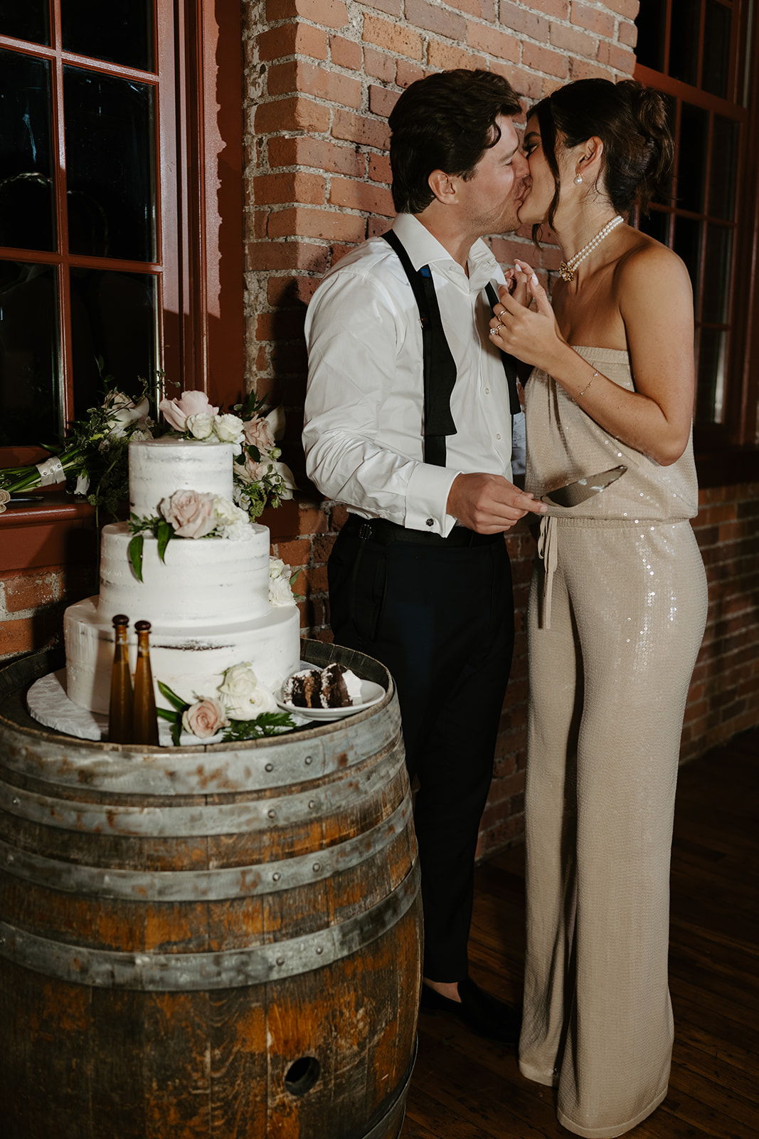 Bride and groom share a sweet kiss after cutting their cake on a wooden barrel.