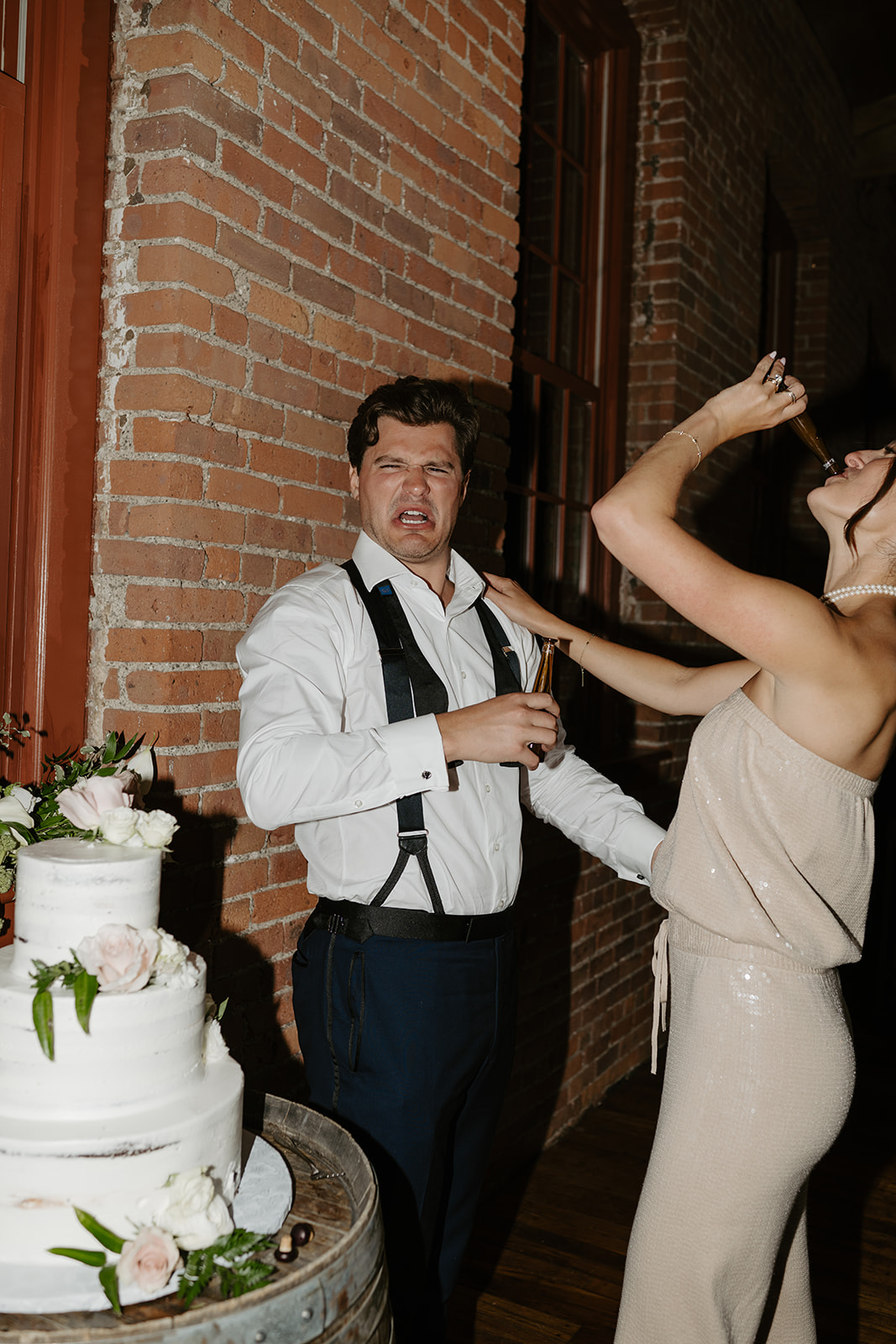 Bride and groom drink celebratory shots next to their cake as the groom makes a funny face.