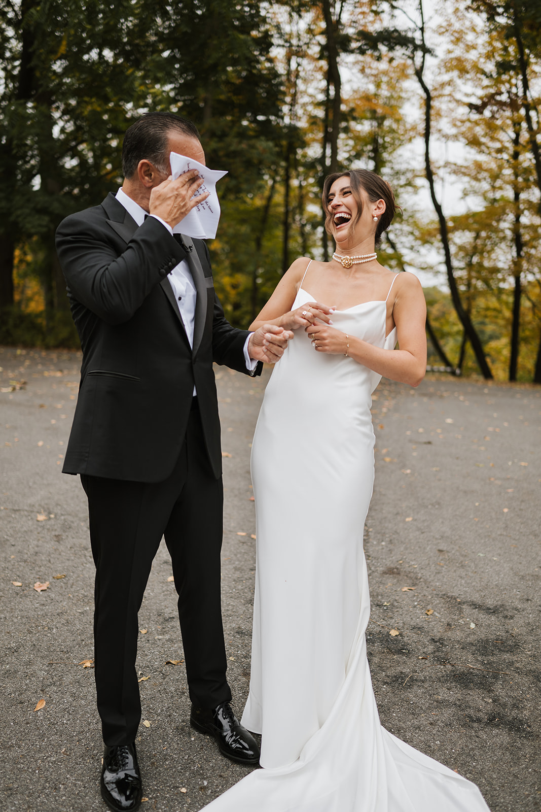 Father wipes a tear as the bride laughs during their emotional first look outdoors.