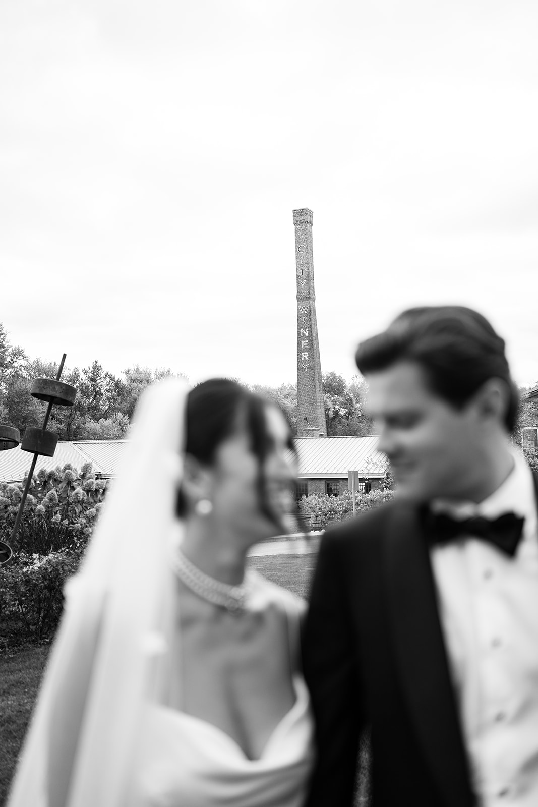 Black and white portrait focusing on the City Winery smokestack with the couple blurred in the foreground.