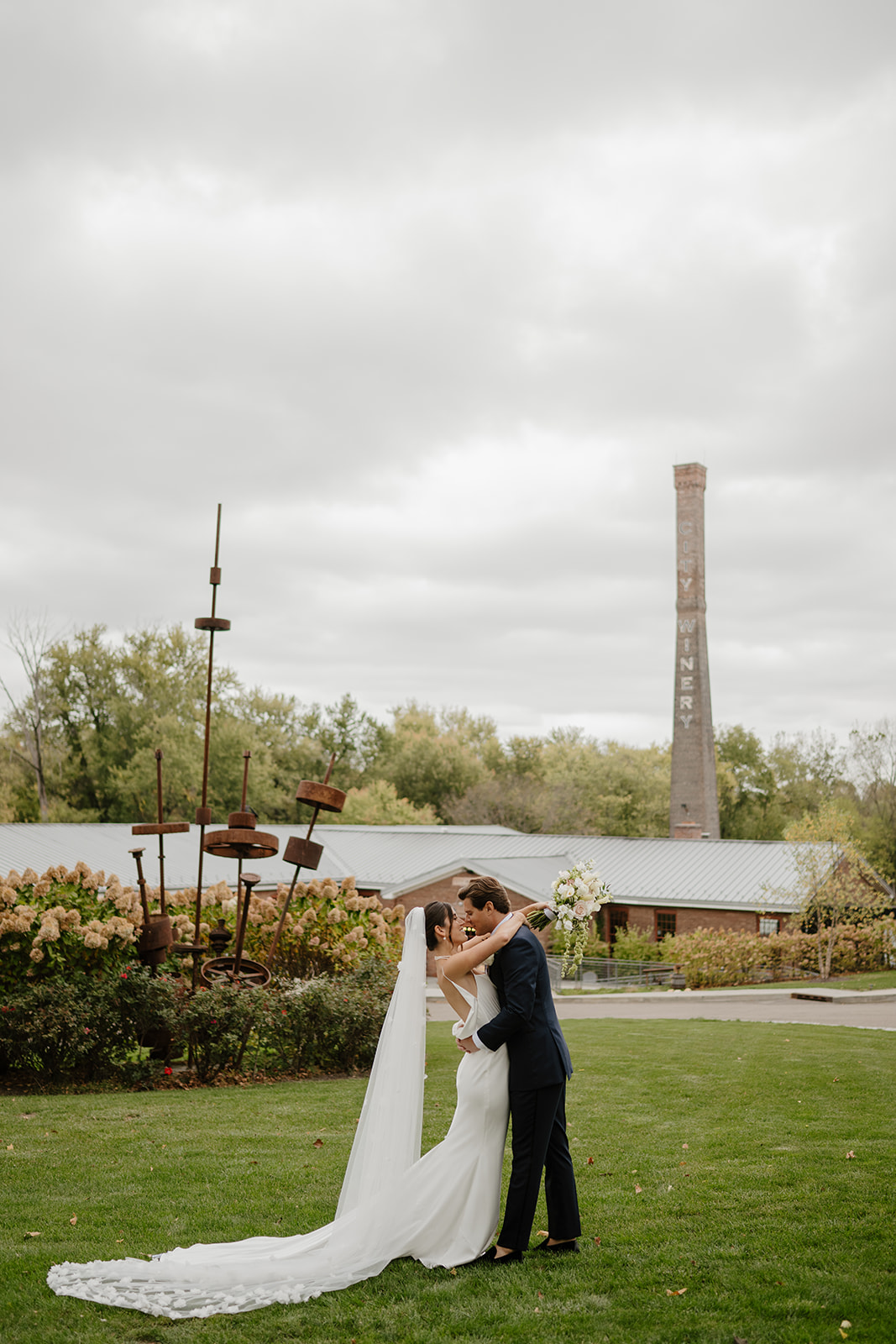 Bride and groom embrace on the lawn, leaning in for a kiss under the overcast sky at City Winery.