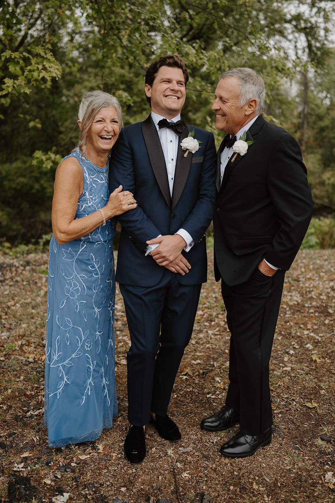 Groom laughs with his parents during pre-ceremony wedding photos in the woods.