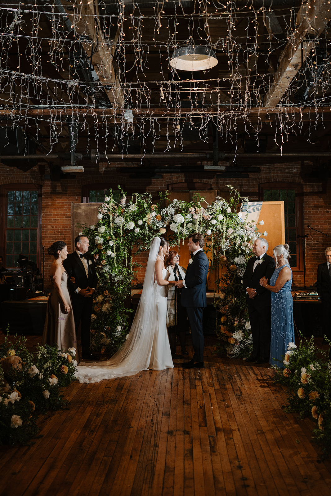 Wide shot of the wedding ceremony under a floral Chuppah and canopy of delicate fairy lights.