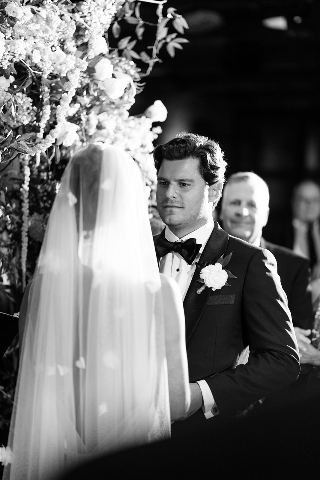 Black and white photo of the groom looking lovingly at the bride during their ceremony vows.