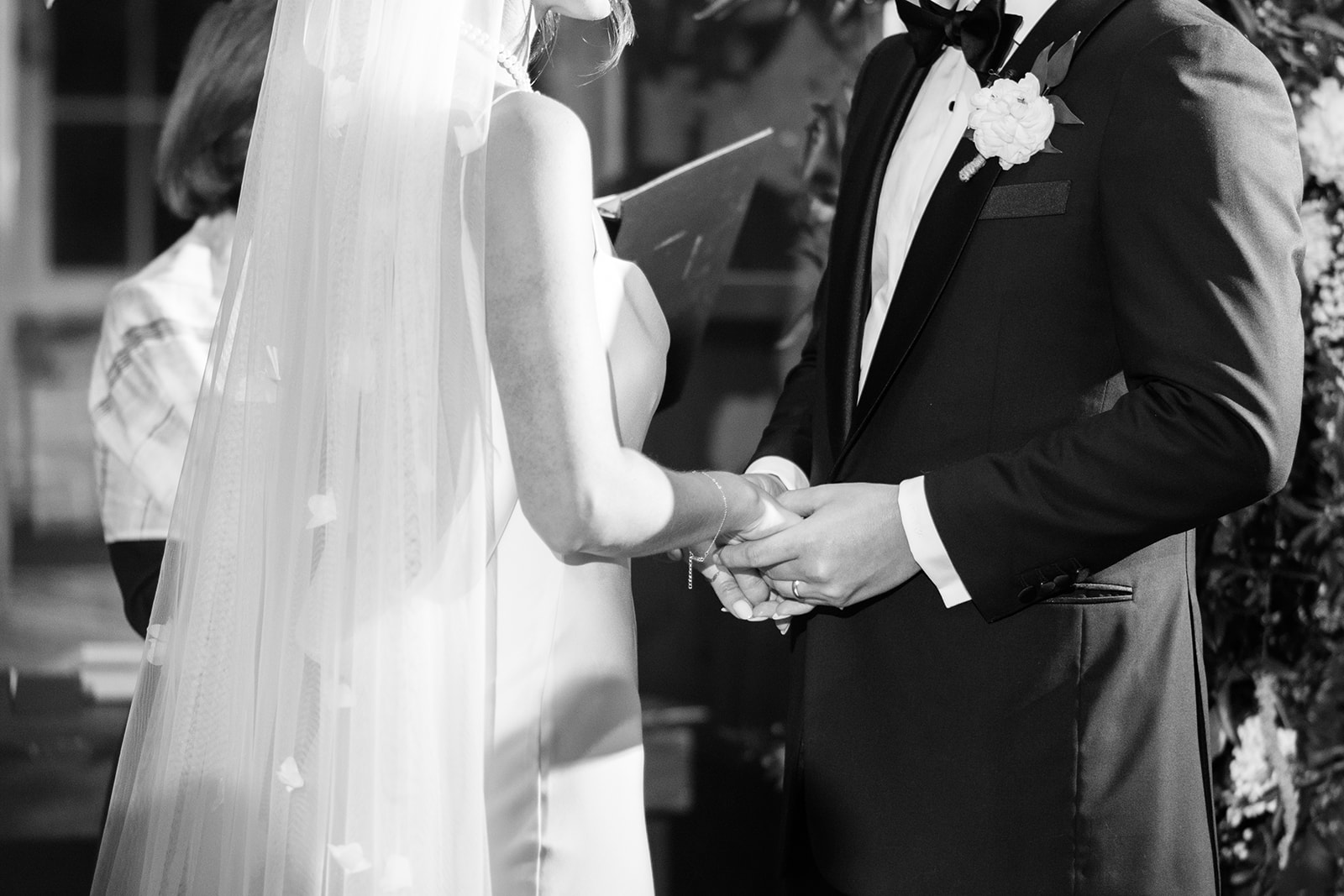 Black and white close-up of the bride and groom holding hands during their marriage ceremony.