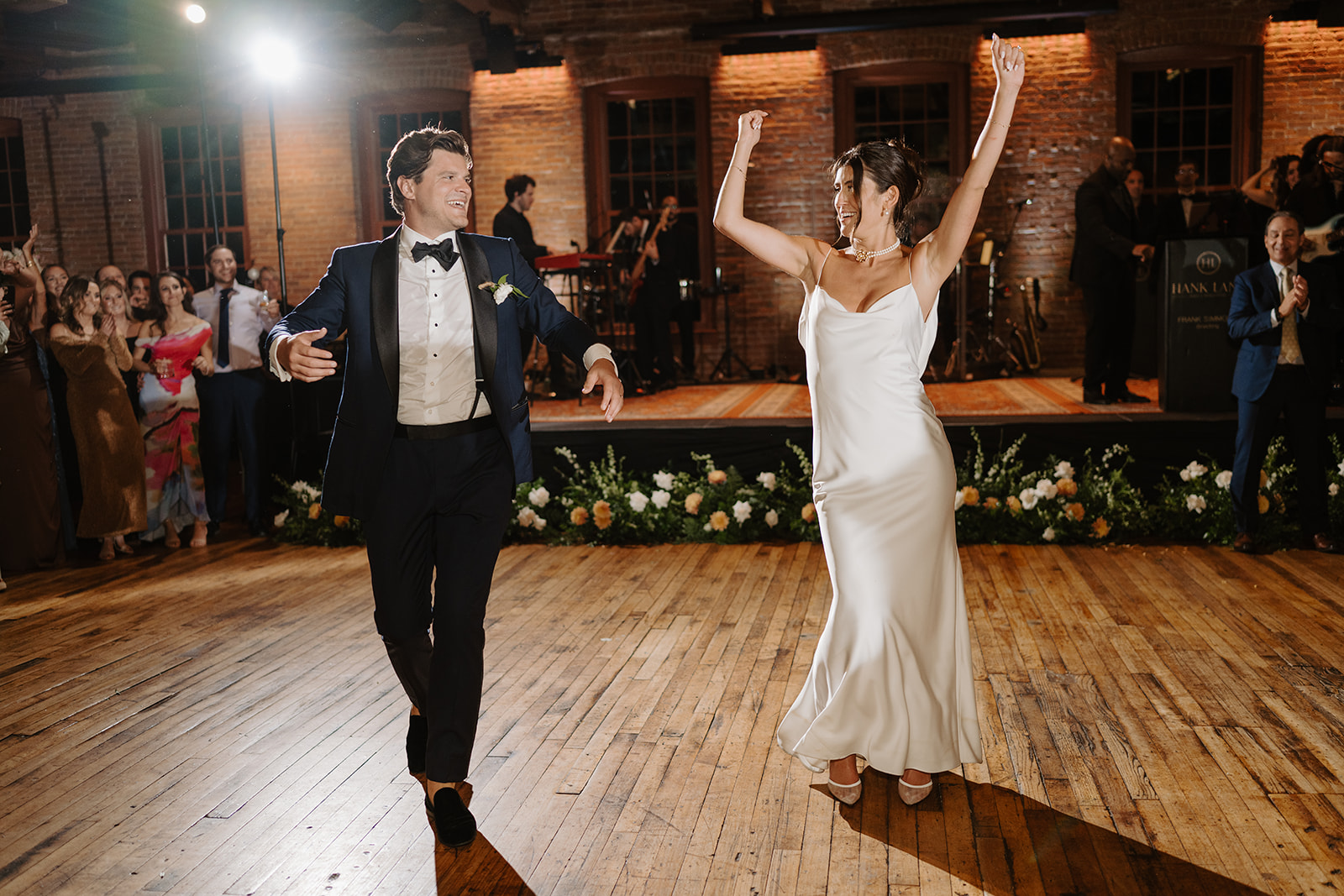 Bride and groom dance joyfully, with the bride raising her arms in celebration on the dance floor.