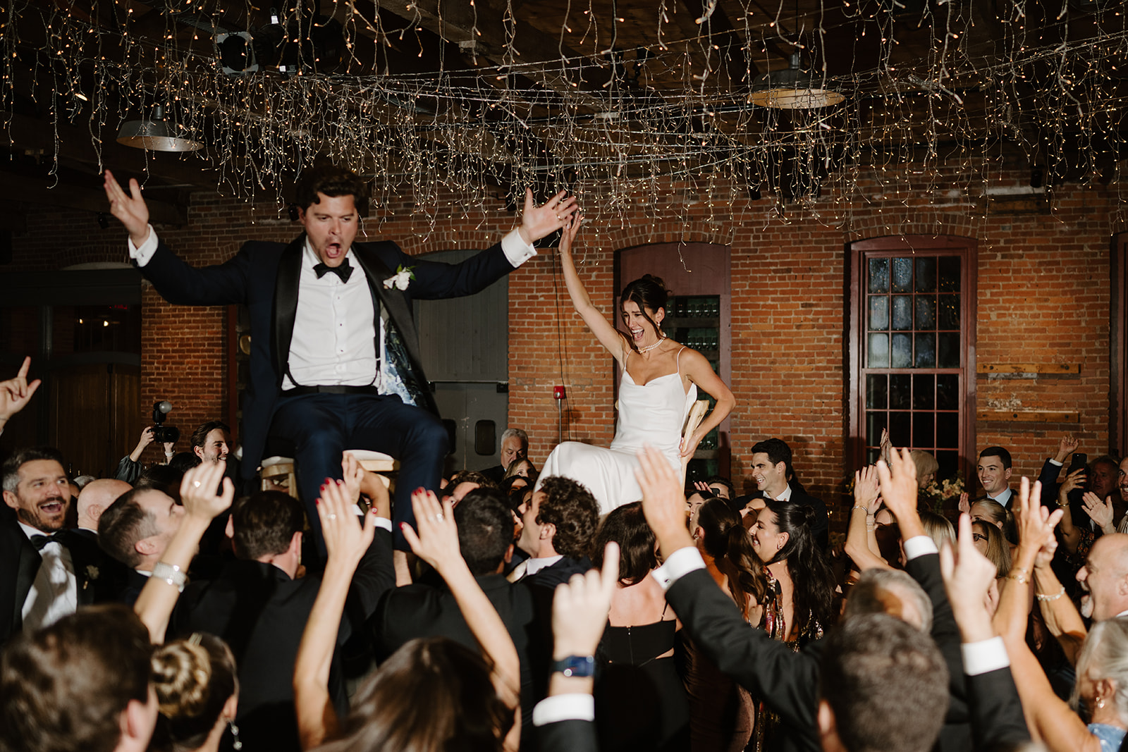 Bride and groom are lifted on chairs during the traditional Hora dance at their lively reception.
